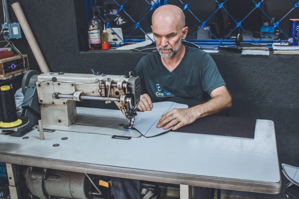 Profissional experiente da CriaCar costurando revestimento em m&aacute;quina industrial